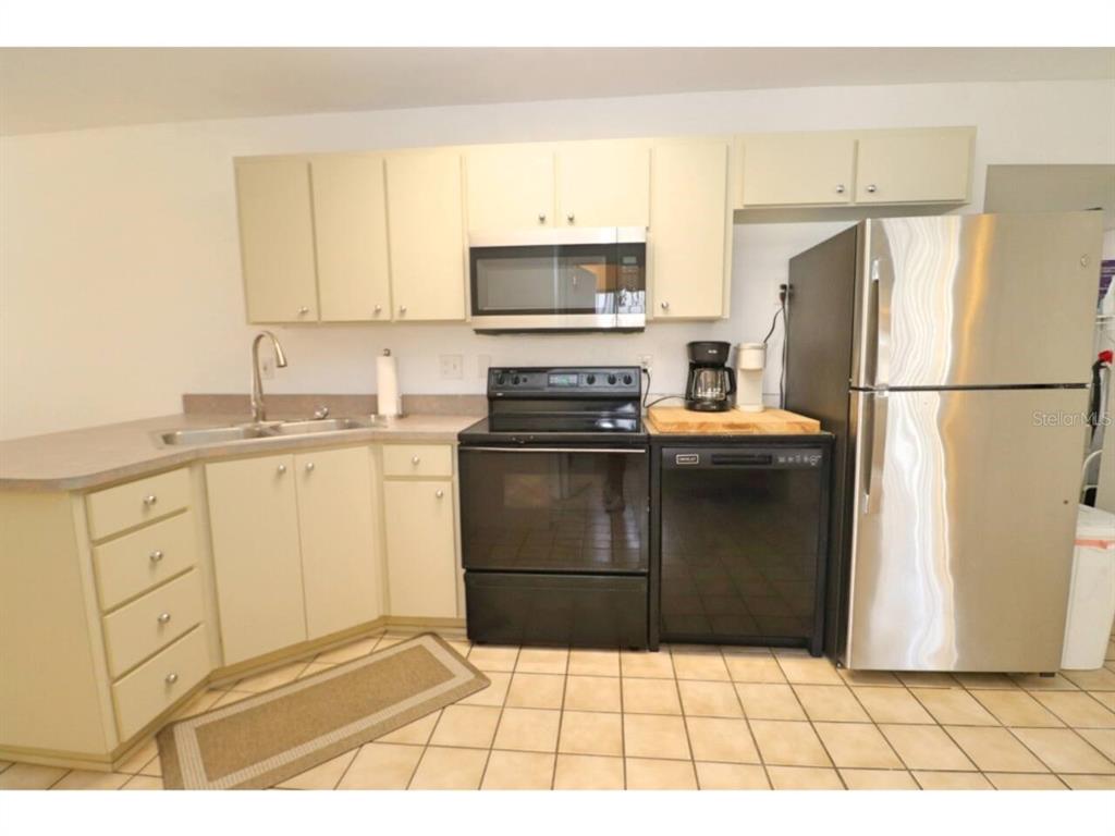A kitchen features light-colored cabinets, a stainless steel refrigerator, a black stove, and tiled flooring — 906 E 11TH AVENUE, NEW SMYRNA BEACH, FL