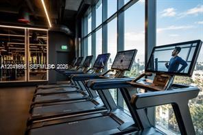A row of treadmills faces floor-to-ceiling windows in a modern gym with dark interior finishes — 20 NE 11th ST # 3207, Miami FL 33132, MIAMI, FL