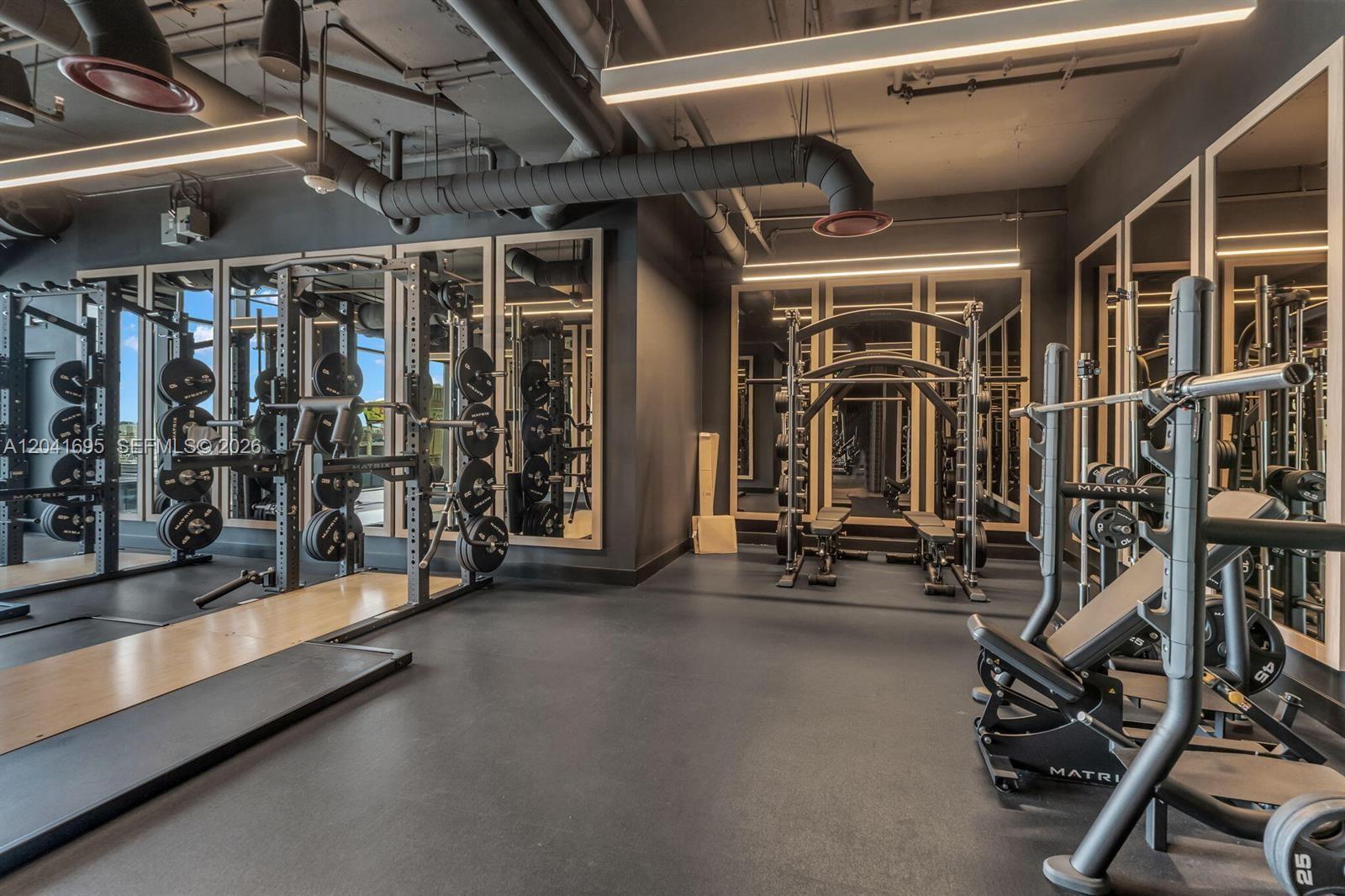 A modern gym features weight racks, mirrors, exposed ductwork, and dark rubber flooring — 20 NE 11th ST # 3207, Miami FL 33132, MIAMI, FL