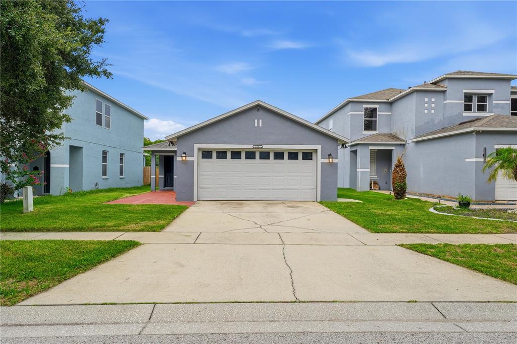 A single-story house with a gray exterior and a two-car garage sits between two-story homes — 5217 MANGO FRUIT STREET, SEFFNER, FL