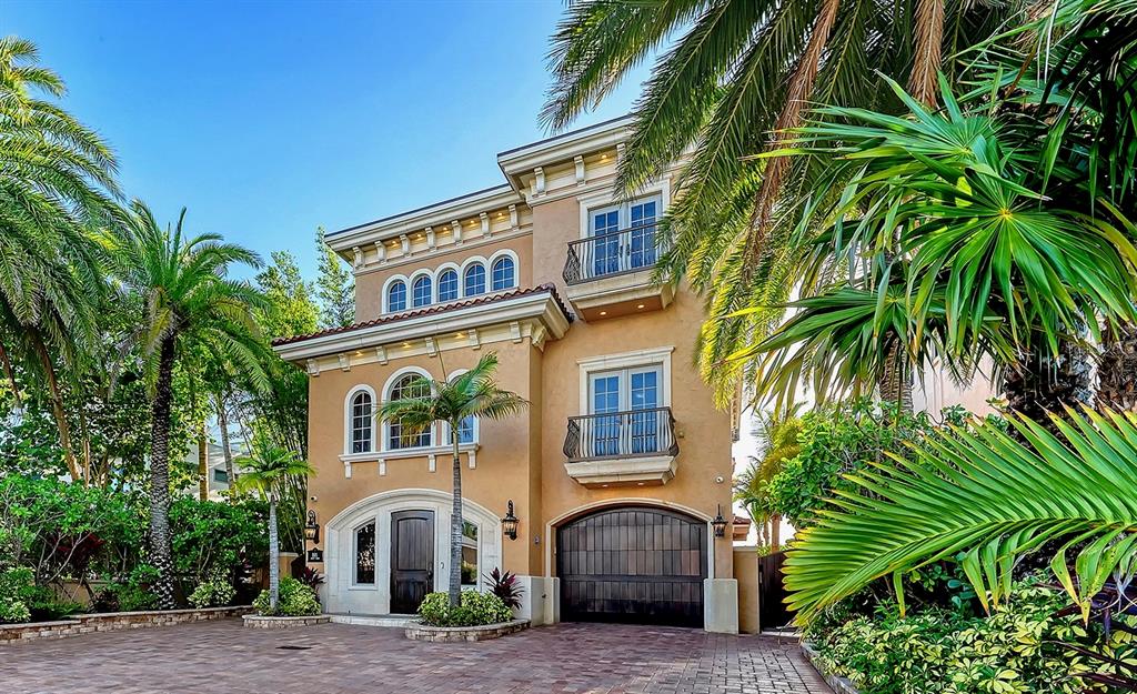 A three-story tan stucco house with a dark wood garage door and palm trees — 801 N SHORE DRIVE, ANNA MARIA, FL