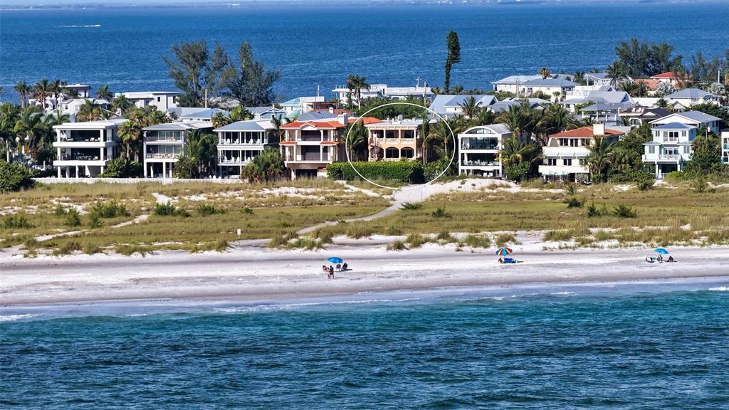 An aerial view shows a multi-story house circled on a beach with nearby coastal homes — 801 N SHORE DRIVE, ANNA MARIA, FL