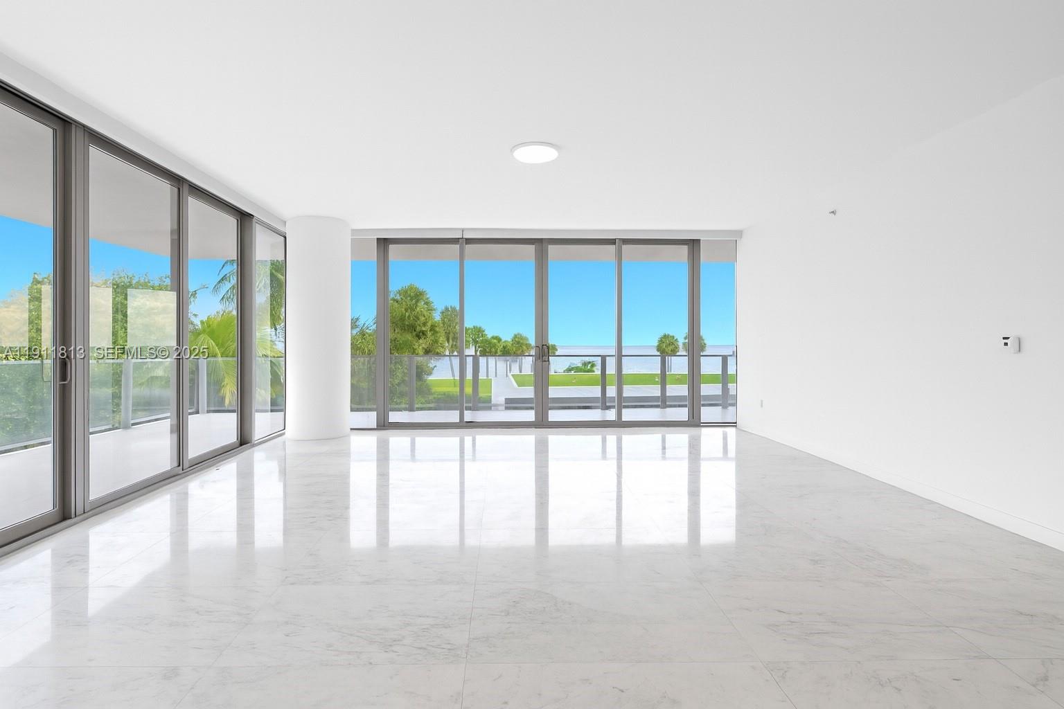 A bright, empty room features white marble floors, floor-to-ceiling glass sliding doors, and water views — 350 E Ocean Dr # 301N, Key Biscayne FL 33149, KEY BISCAYNE, FL