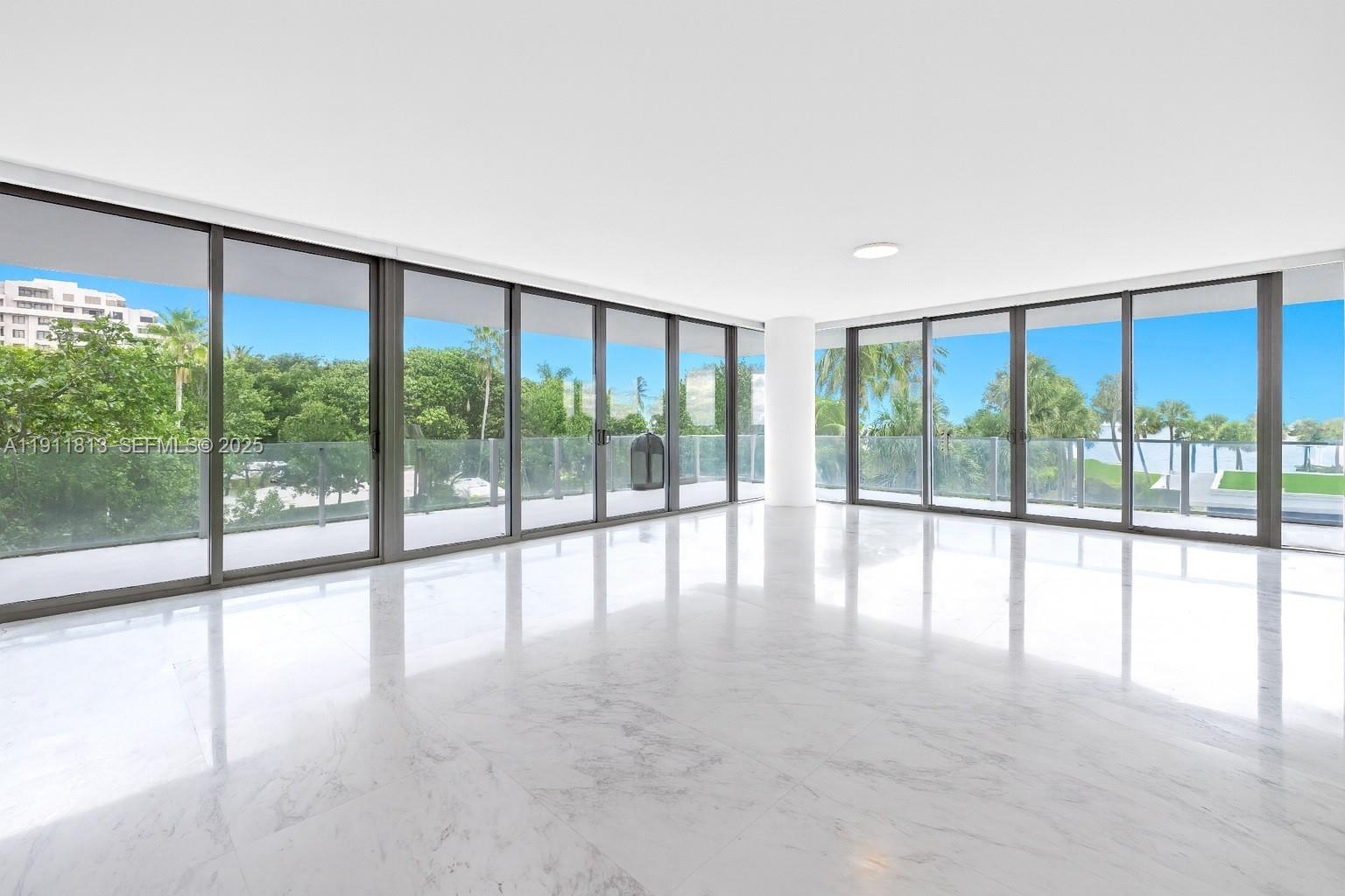 A bright, empty room features white marble floors and floor-to-ceiling glass walls overlooking trees — 350 E Ocean Dr # 301N, Key Biscayne FL 33149, KEY BISCAYNE, FL