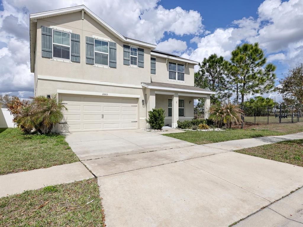A two-story beige house with a two-car garage and gray shutters under a cloudy sky — 10003 GEESE TRAIL CIRCLE, SUN CITY CENTER, FL