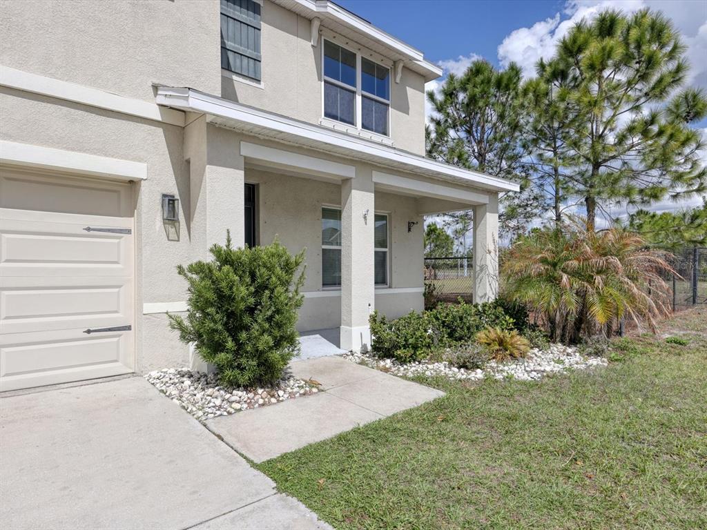 A two-story house exterior features a beige stucco facade, a garage, and a covered porch — 10003 GEESE TRAIL CIRCLE, SUN CITY CENTER, FL