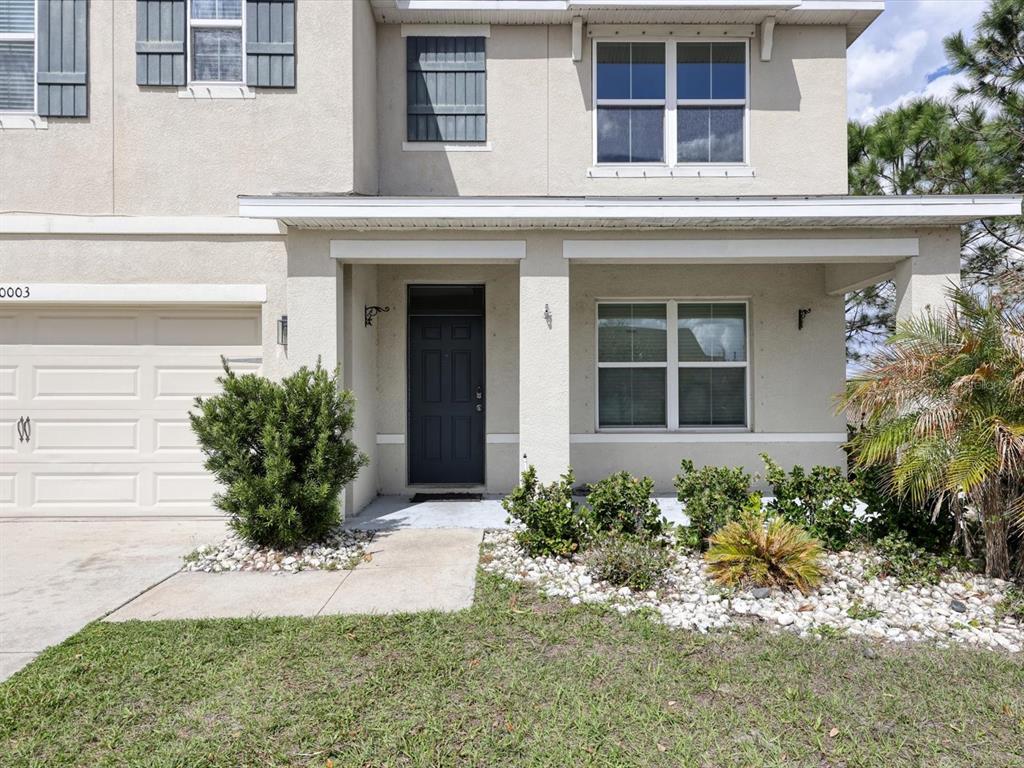 The exterior of a two-story house features a covered porch, a garage, and landscaping — 10003 GEESE TRAIL CIRCLE, SUN CITY CENTER, FL