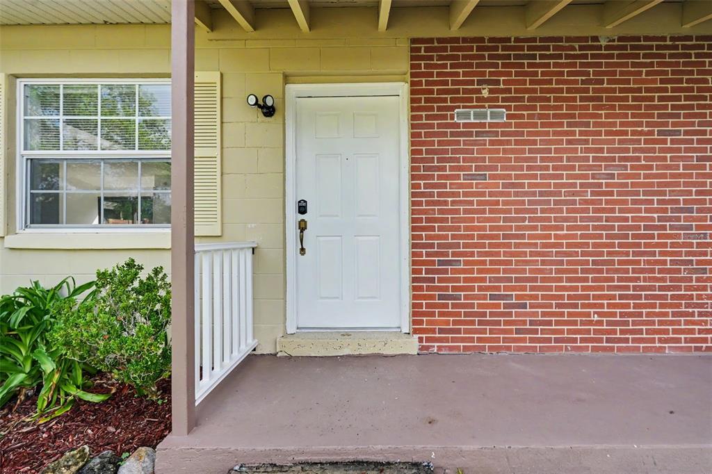 A white front door is centered on a porch with brick and painted block walls — 9447 N MILAM WAY, CITRUS SPRINGS, FL