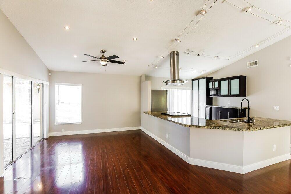 A kitchen with granite countertops and dark cabinets overlooks an open living area with hardwood floors — PEMBROKE PINES, FL