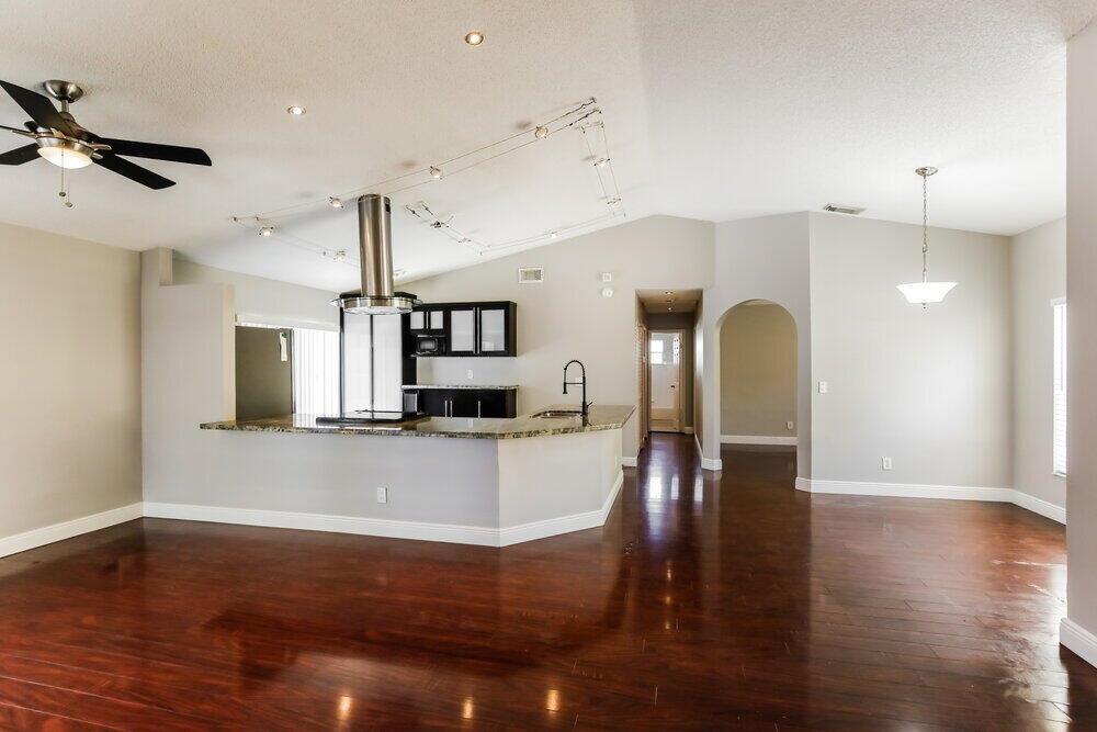 A kitchen with dark cabinets and granite countertops overlooks a spacious living area with hardwood floors — PEMBROKE PINES, FL