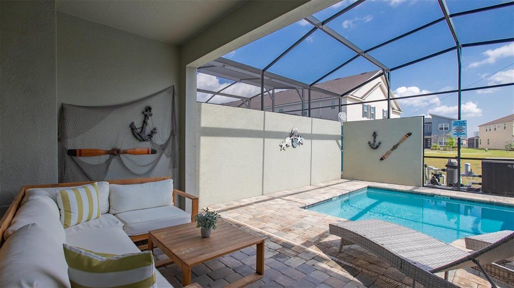 A covered patio features a seating area, a small pool, and nautical wall decor — 2147 COOPER BELL PLACE, KISSIMMEE, FL