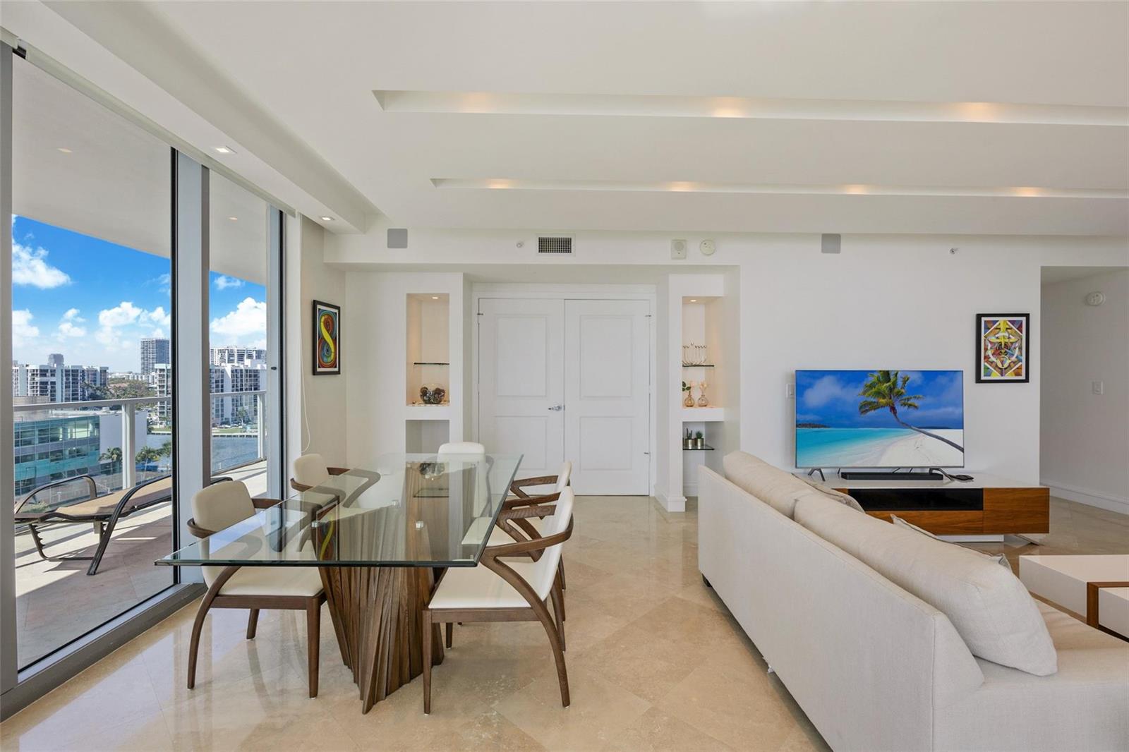 A modern living and dining area with a glass table, beige sofa, and balcony view — 3101 S Ocean Drive # 902, Hollywood FL 33019, HOLLYWOOD, FL