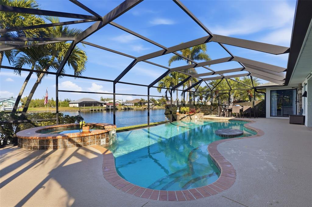 A screened-in pool and hot tub overlook a canal with palm trees in the background — 15508 RUSTON CIRCLE, PORT CHARLOTTE, FL