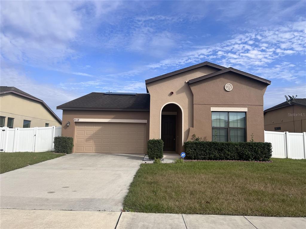 A single-story suburban house with a tan stucco exterior, a two-car garage, and white fencing — 3113 HARRIS PARK WAY, KISSIMMEE, FL