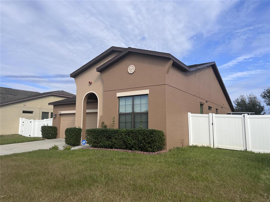 A single-story tan house with a brown roof, a garage, and a white vinyl fence — 3113 HARRIS PARK WAY, KISSIMMEE, FL