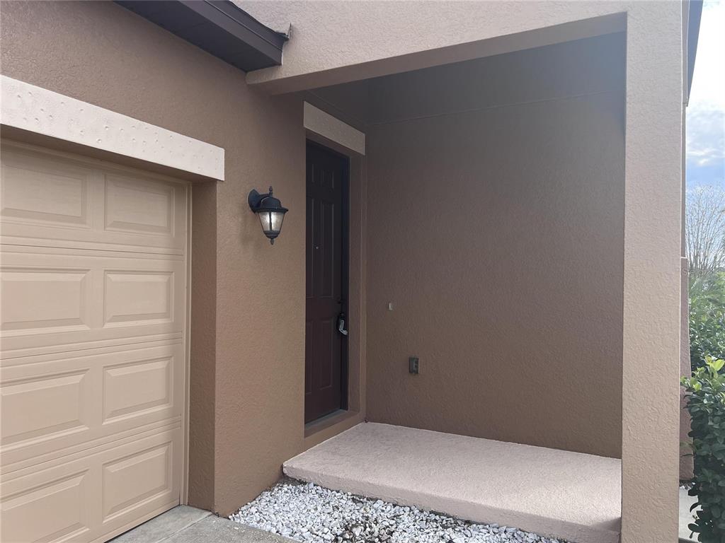 A brown exterior wall features a tan garage door, a dark front door, and porch — 3113 HARRIS PARK WAY, KISSIMMEE, FL