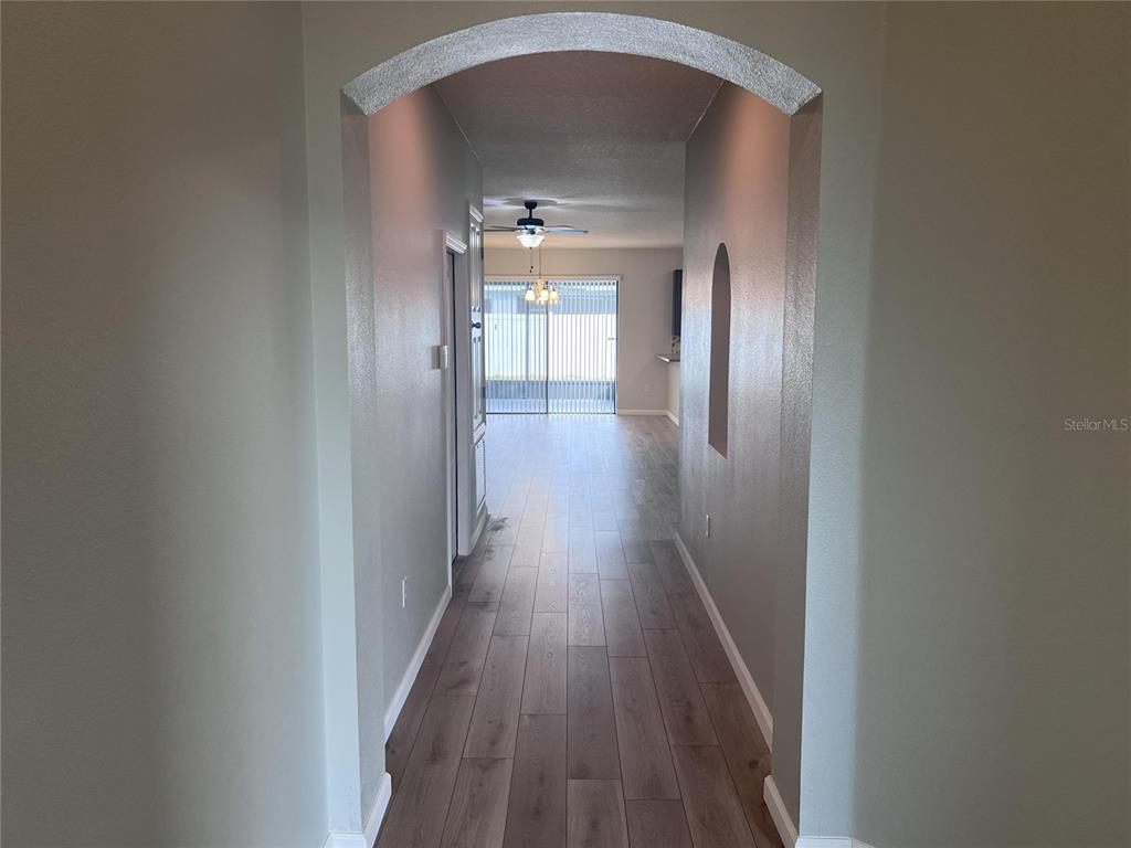 A hallway with wood-look flooring leads to an open living area with sliding glass doors — 3113 HARRIS PARK WAY, KISSIMMEE, FL