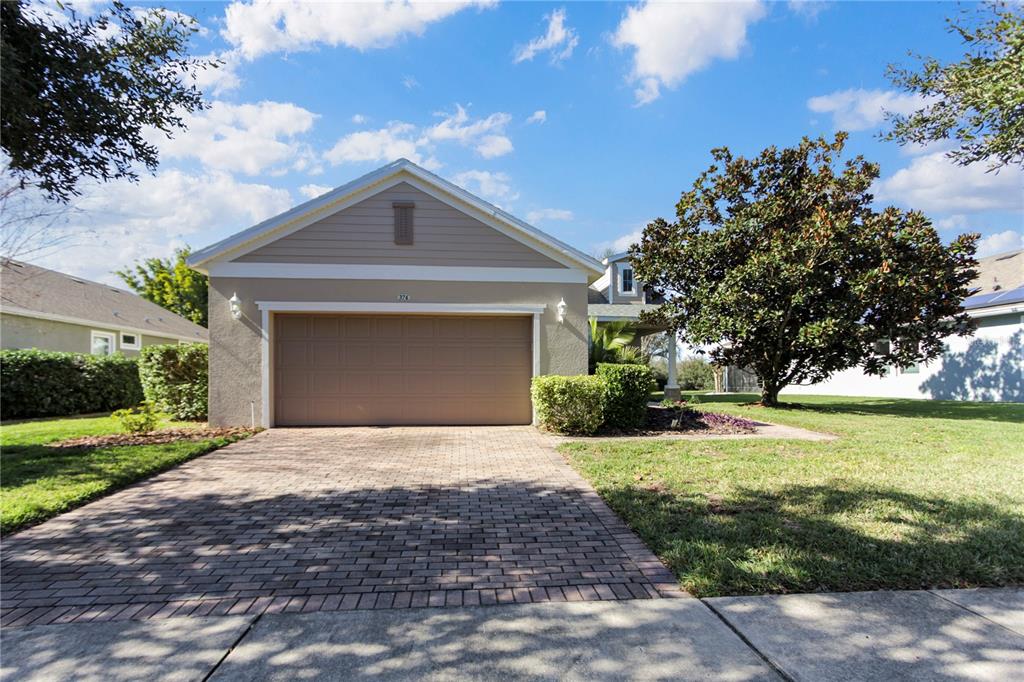 A tan house features a two-car garage, a brick paver driveway, and a large tree — 374 SALT MARSH LANE, GROVELAND, FL
