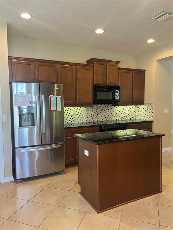 A kitchen features dark wood cabinets, stainless steel appliances, a granite island, and tiled floors — 374 SALT MARSH LANE, GROVELAND, FL