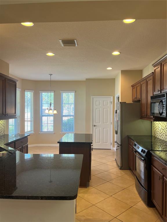 A kitchen features dark wood cabinets, granite countertops, stainless steel appliances, and tile flooring — 374 SALT MARSH LANE, GROVELAND, FL