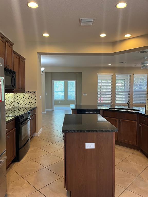 A kitchen features dark wood cabinets, black granite countertops, and tile flooring — 374 SALT MARSH LANE, GROVELAND, FL