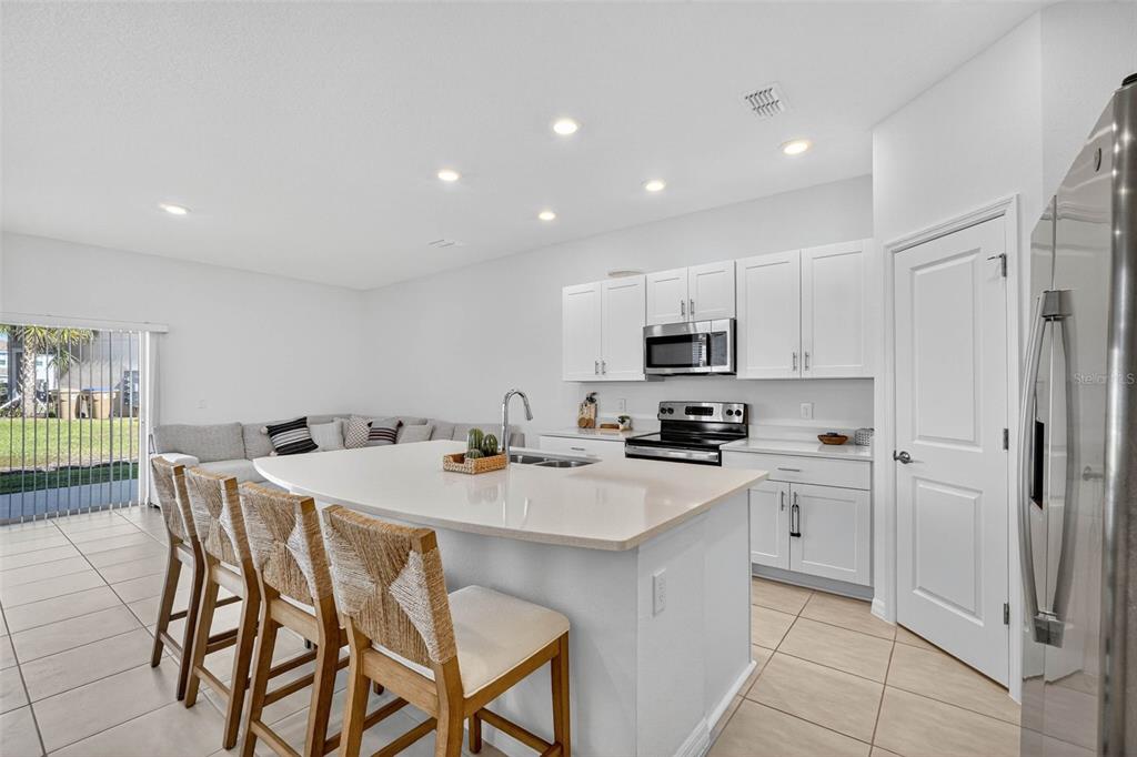 A modern kitchen with white cabinets, a large island, and an adjacent living area — 3607 MAIN HARBOR DRIVE, KISSIMMEE, FL