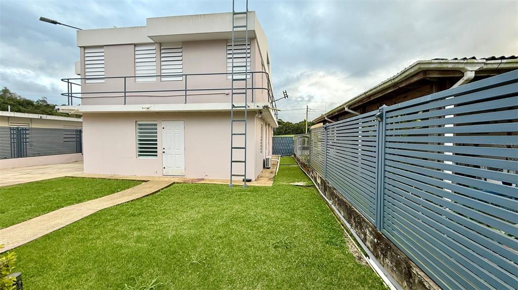 A two-story light-colored house features a metal ladder, a balcony, and a slatted privacy fence — WD Colina de Lourdes FLORIDA AFUERA WD COLINAS DE LOURDES SECTOR LOT 4, BARCELONETA, PR