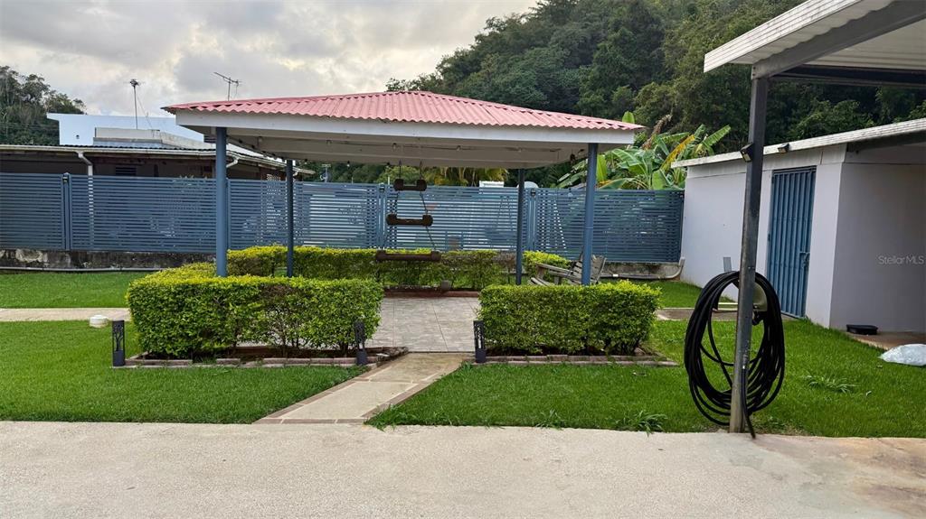 A covered patio with a tiled floor and a wooden swing sits in a backyard — WD Colina de Lourdes FLORIDA AFUERA WD COLINAS DE LOURDES SECTOR LOT 4, BARCELONETA, PR