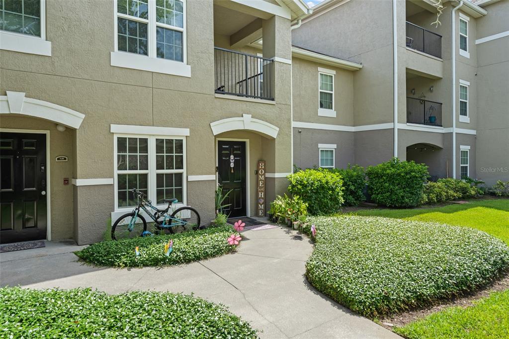 An exterior view of a multi-story apartment building with a sidewalk and landscaping — 6554 SWISSCO DRIVE UNIT 518, ORLANDO, FL