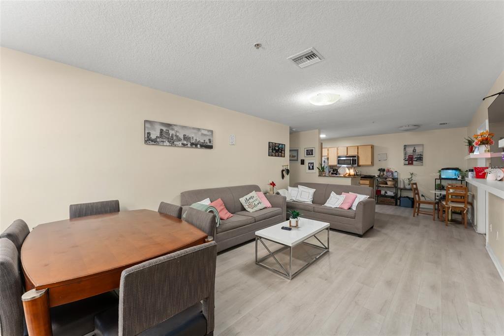 A living room and dining area with light wood-look flooring, gray sofas, and a table — 6554 SWISSCO DRIVE UNIT 518, ORLANDO, FL