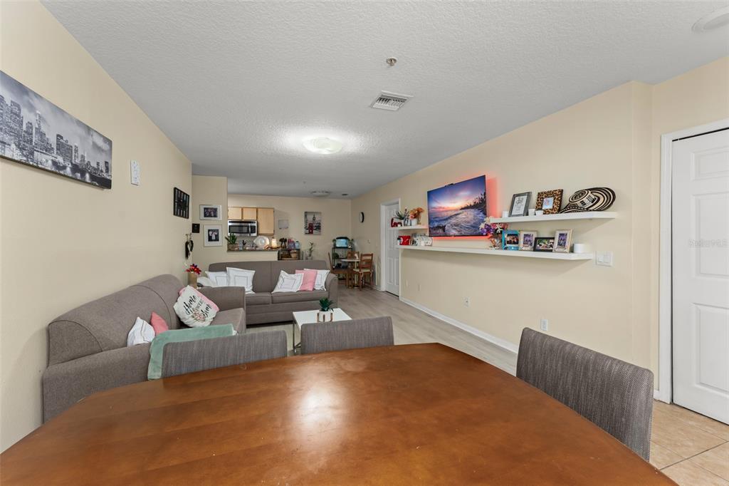 A living room with a grey sofa, a wall-mounted television, and a wooden dining table — 6554 SWISSCO DRIVE UNIT 518, ORLANDO, FL