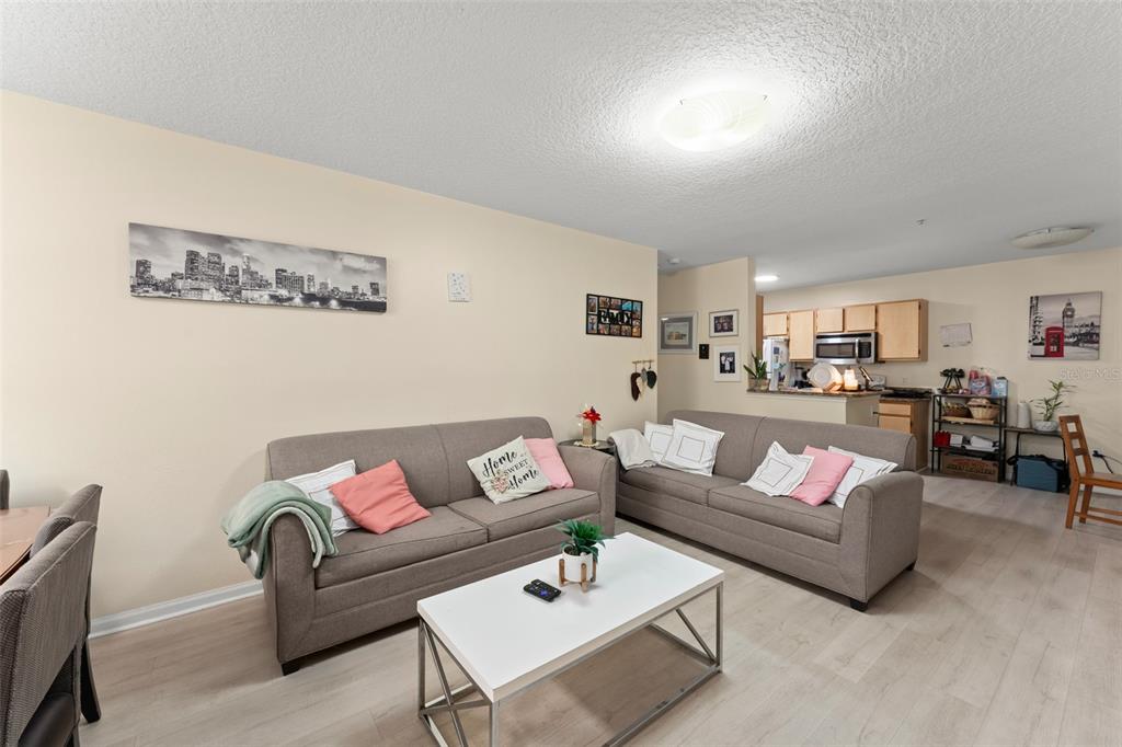 A living room with two gray sofas, a white coffee table, and an open kitchen — 6554 SWISSCO DRIVE UNIT 518, ORLANDO, FL