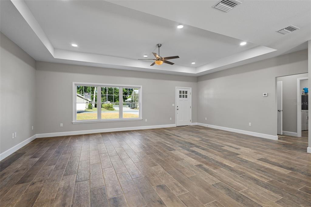 A spacious living room features light gray walls, wood-look tile flooring, and a tray ceiling — 9100 DORIE DRIVE, TRENTON, FL