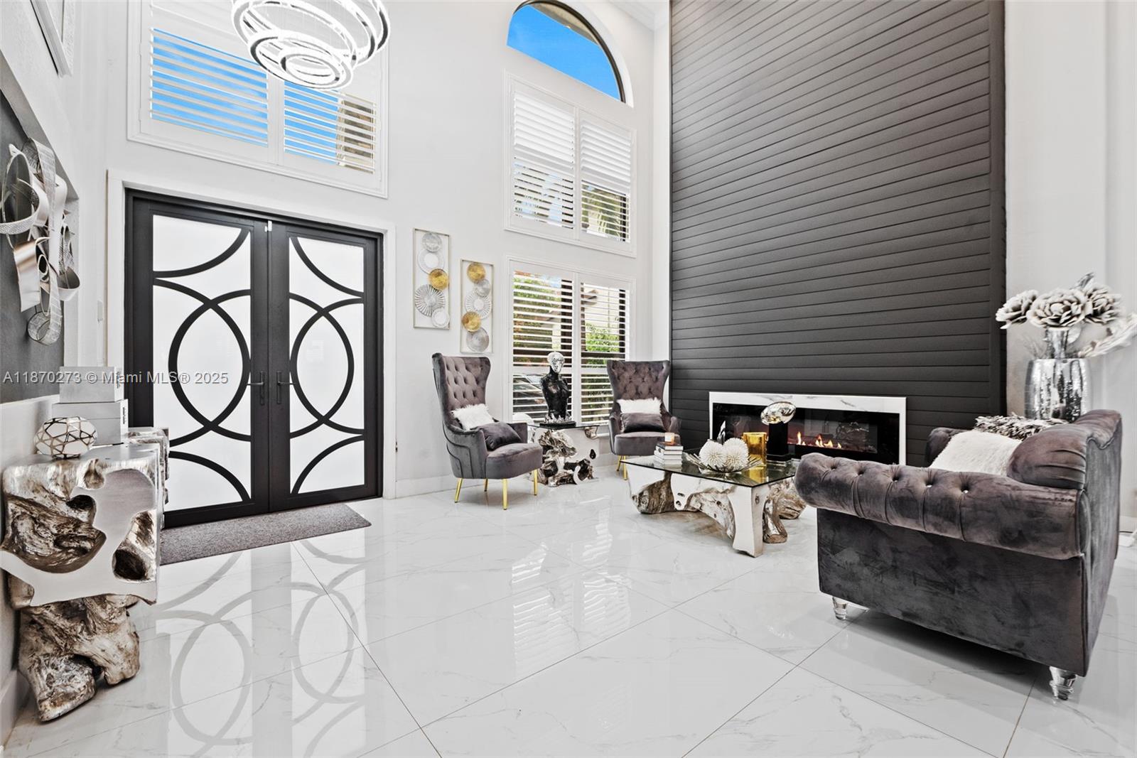 A modern living room features high ceilings, a dark paneled fireplace wall, and white flooring — 3591 SW 177th Ave, Miramar FL 33029, MIRAMAR, FL