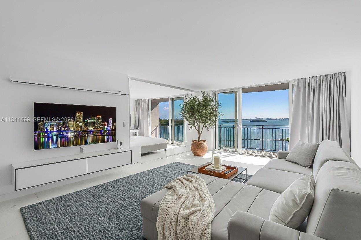 A modern living room features a large television, gray sectional sofa, and balcony water views — 770 NE 69th St # 6C, Miami FL 33138, MIAMI, FL