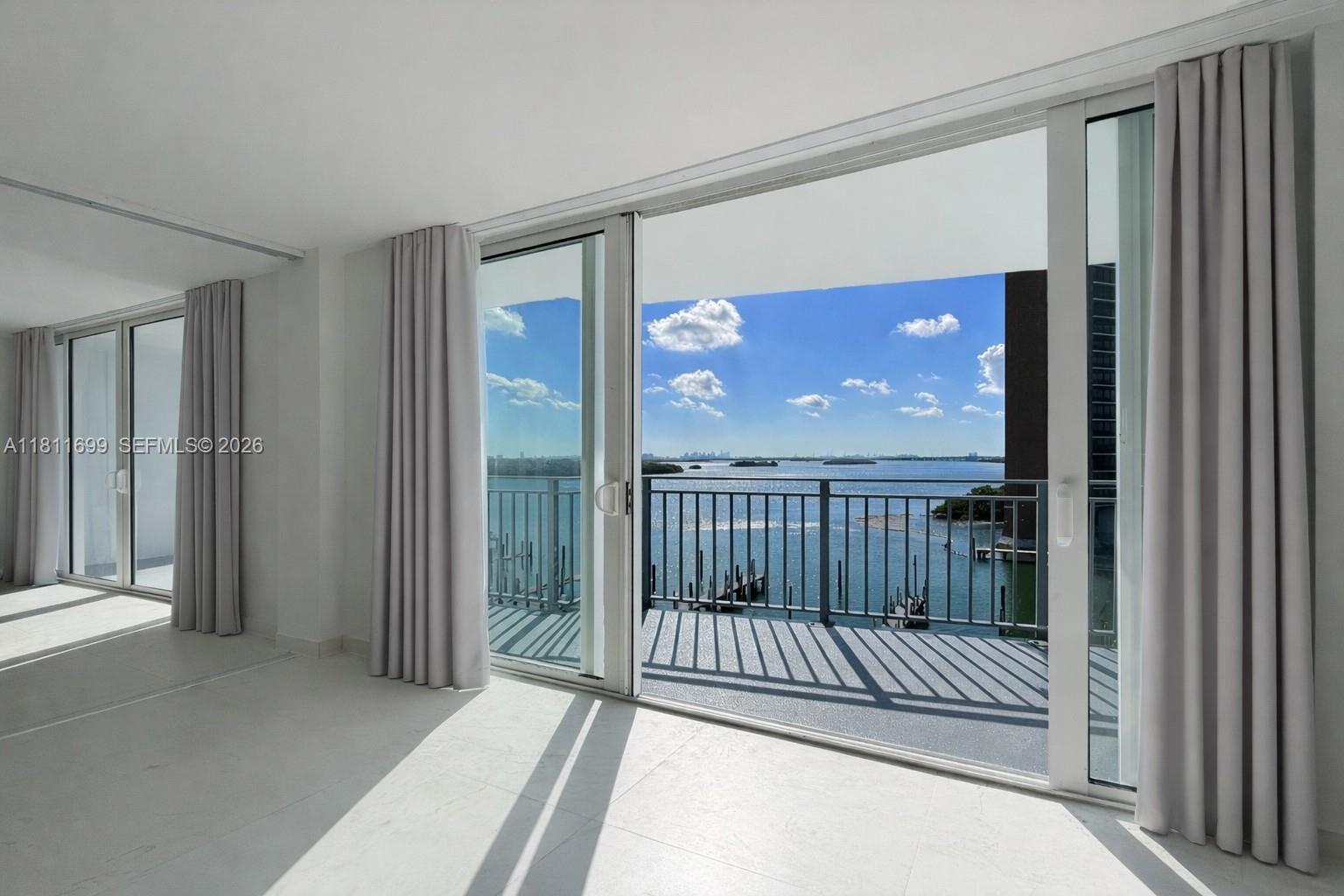 A bright room with white tile floors features sliding glass doors opening to a waterfront balcony — 770 NE 69th St # 6C, Miami FL 33138, MIAMI, FL