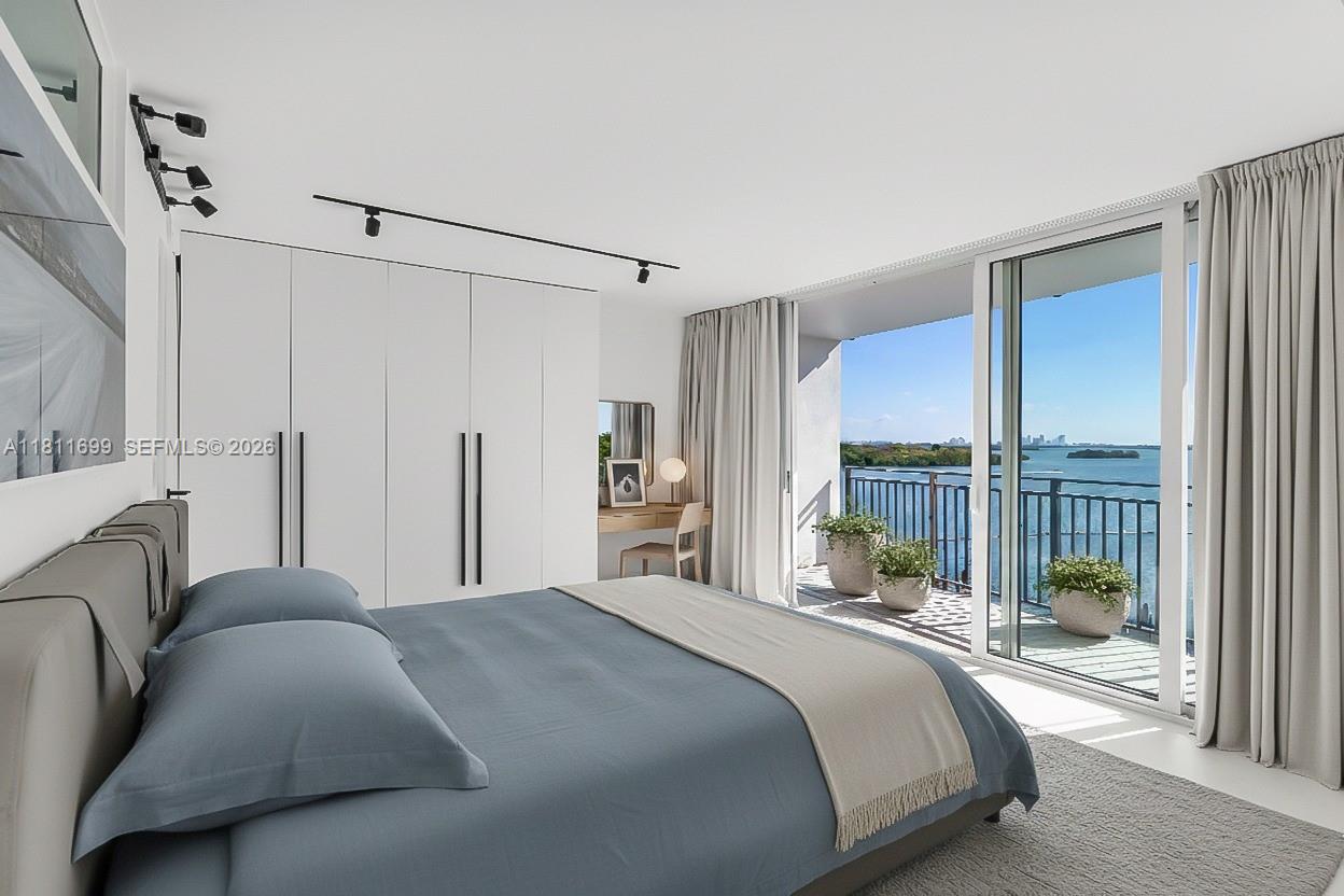 A modern bedroom features a blue bed, white wardrobes, and a balcony overlooking the water — 770 NE 69th St # 6C, Miami FL 33138, MIAMI, FL