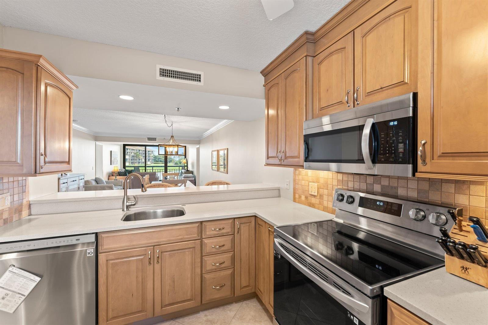 A kitchen with wood cabinets, stainless steel appliances, and a pass-through window to the living area — 601 S Seas Drive # 203, Jupiter FL 33477, JUPITER, FL