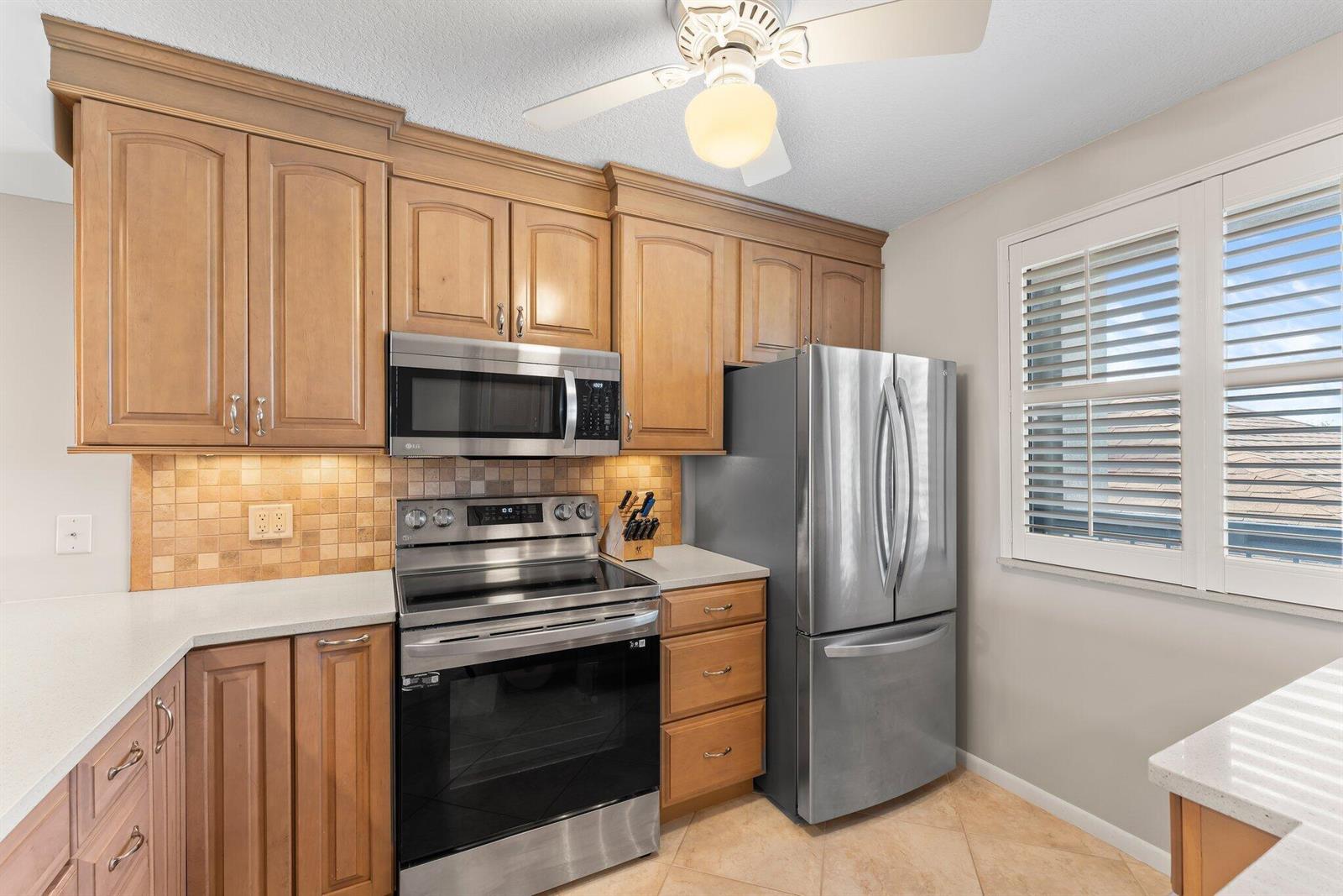 A kitchen features wood cabinets, stainless steel appliances, a tiled backsplash, and a ceiling fan — 601 S Seas Drive # 203, Jupiter FL 33477, JUPITER, FL