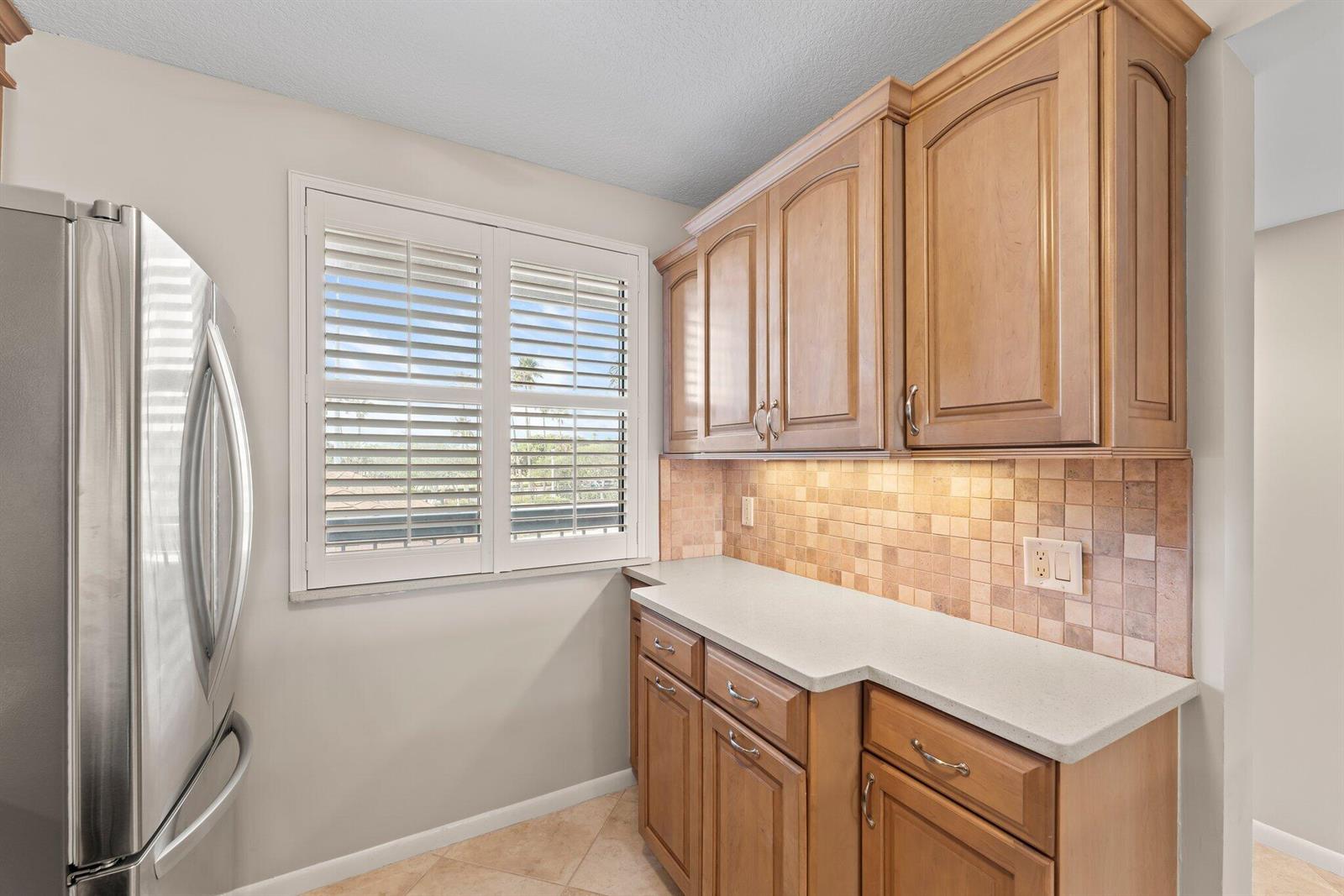 A kitchen corner features wood cabinets, a light countertop, tiled backsplash, and a window with shutters — 601 S Seas Drive # 203, Jupiter FL 33477, JUPITER, FL
