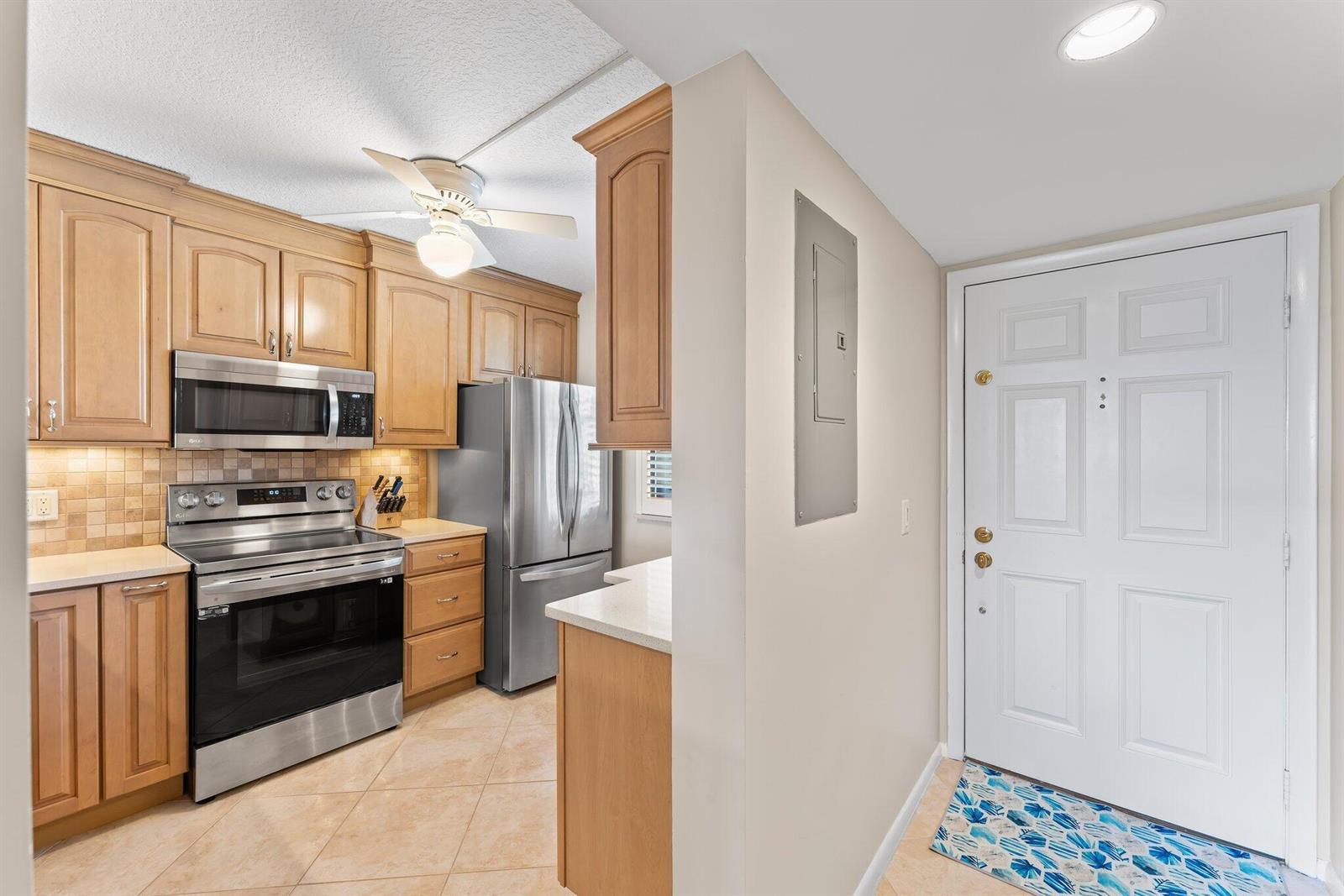 A kitchen with light wood cabinets, stainless steel appliances, and tile flooring near an entryway — 601 S Seas Drive # 203, Jupiter FL 33477, JUPITER, FL