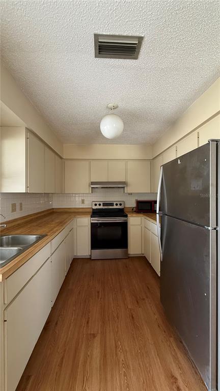 A galley kitchen features beige cabinets, wood-look flooring, a stainless steel stove, and a refrigerator — 201 SAN MARCO AVENUE UNIT 2, NORTH PORT, FL
