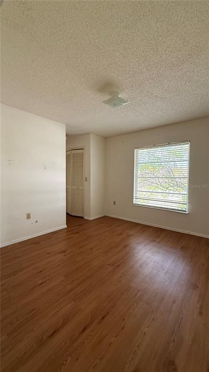 An empty bedroom features wood-look flooring, a textured ceiling, and a window with blinds — 201 SAN MARCO AVENUE UNIT 2, NORTH PORT, FL
