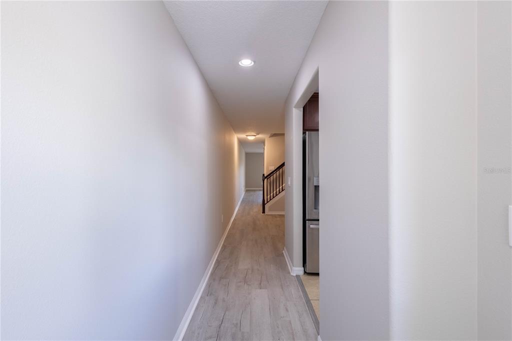 A hallway with light wood-look flooring leads toward a staircase and a kitchen area — 10956 BRICKSIDE COURT, RIVERVIEW, FL
