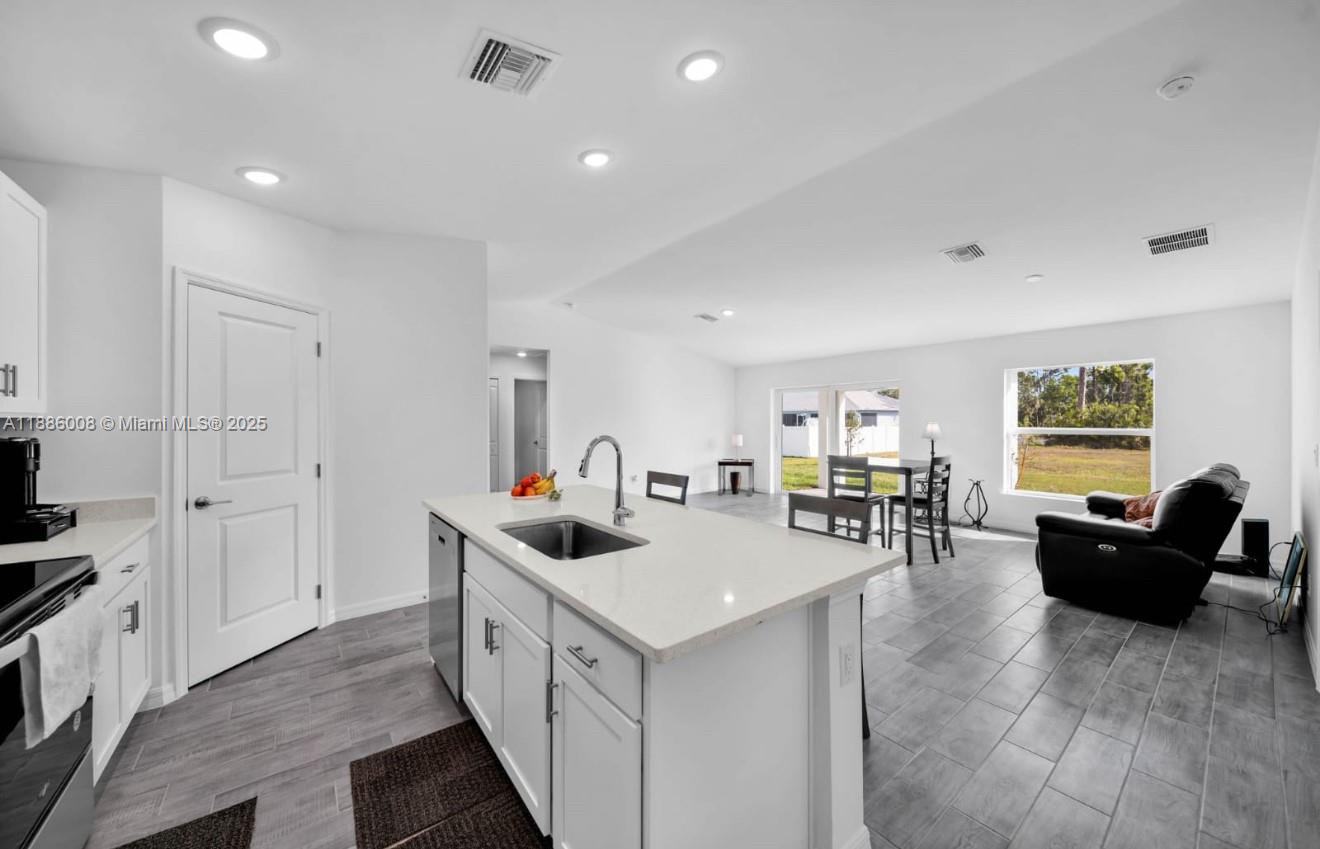 A modern kitchen with a white island and gray tile flooring opens into a living area — 4217 NE 23rd Pl, Cape Coral FL 33909, CAPE CORAL, FL