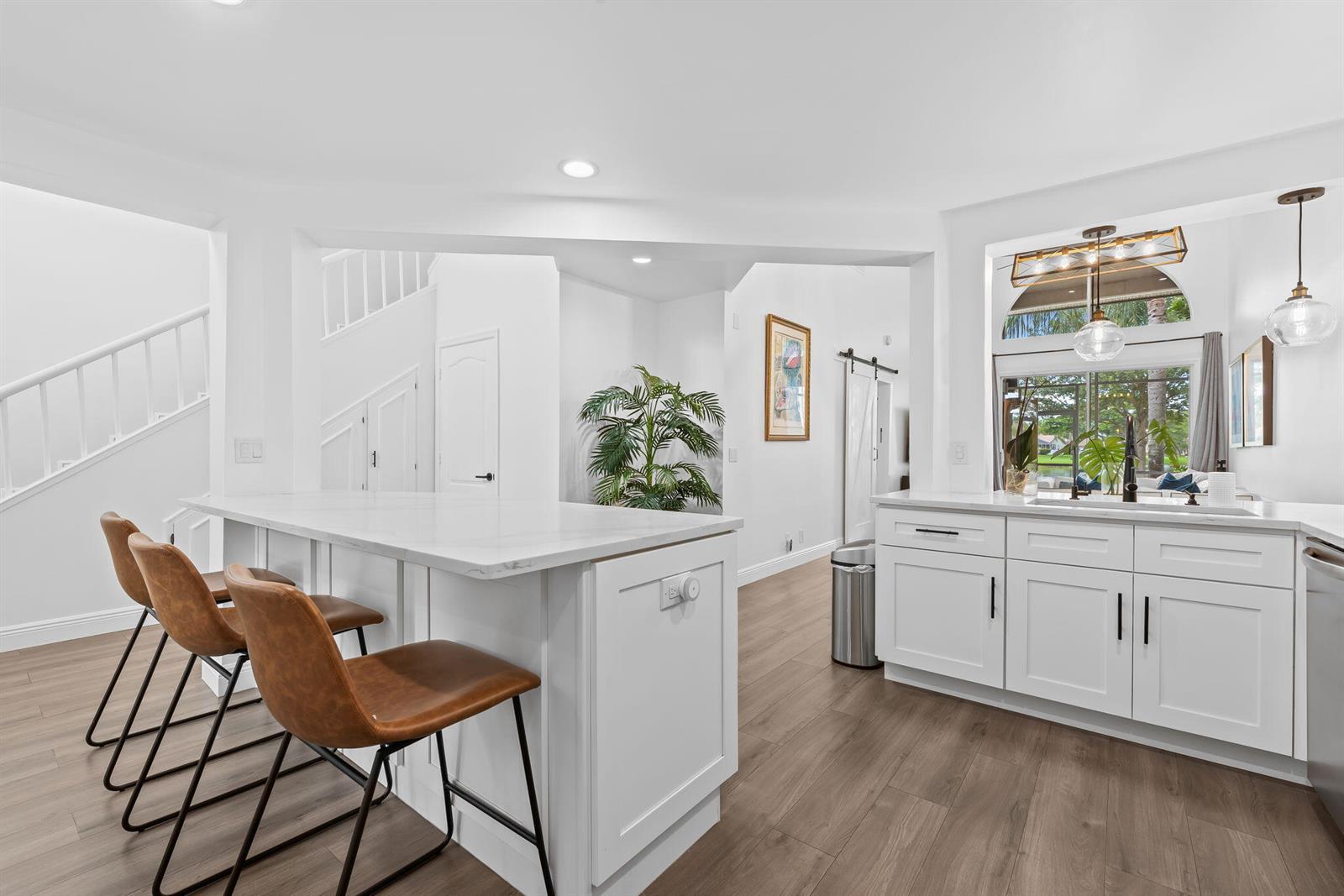 A modern kitchen features white cabinets, a marble-topped island with bar stools, and wood flooring — 9226 Boca Gardens Parkway, Boca Raton FL 33496, BOCA RATON, FL