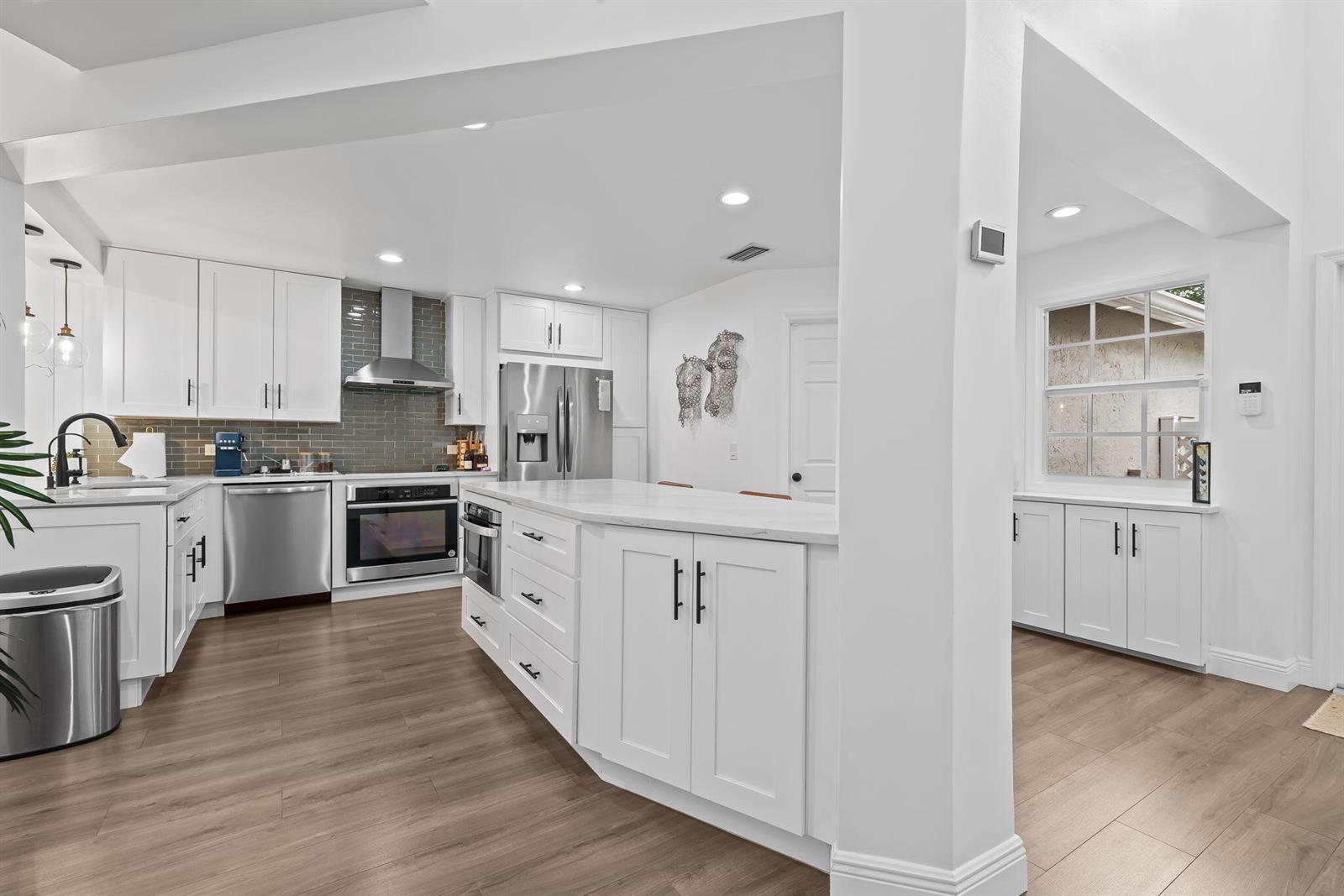 A modern white kitchen features stainless steel appliances, a gray tile backsplash, and wood flooring — 9226 Boca Gardens Parkway, Boca Raton FL 33496, BOCA RATON, FL