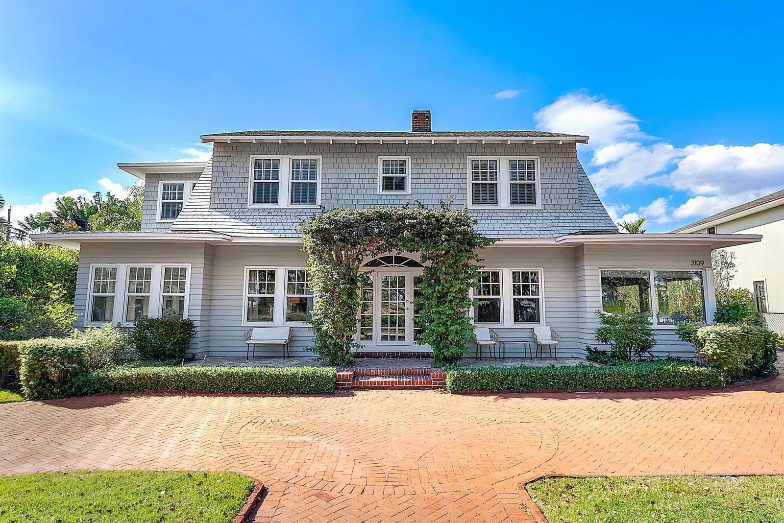 A two-story gray shingled house features a brick driveway and a vine-covered entryway — 3109 Washington Road, West Palm Beach FL 33405, WEST PALM BEACH, FL