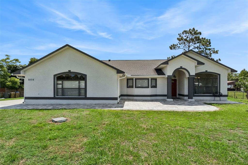 A single-story house with a white stucco exterior, dark trim, and a paved front patio — 7035 BIG BEND DRIVE, ST CLOUD, FL