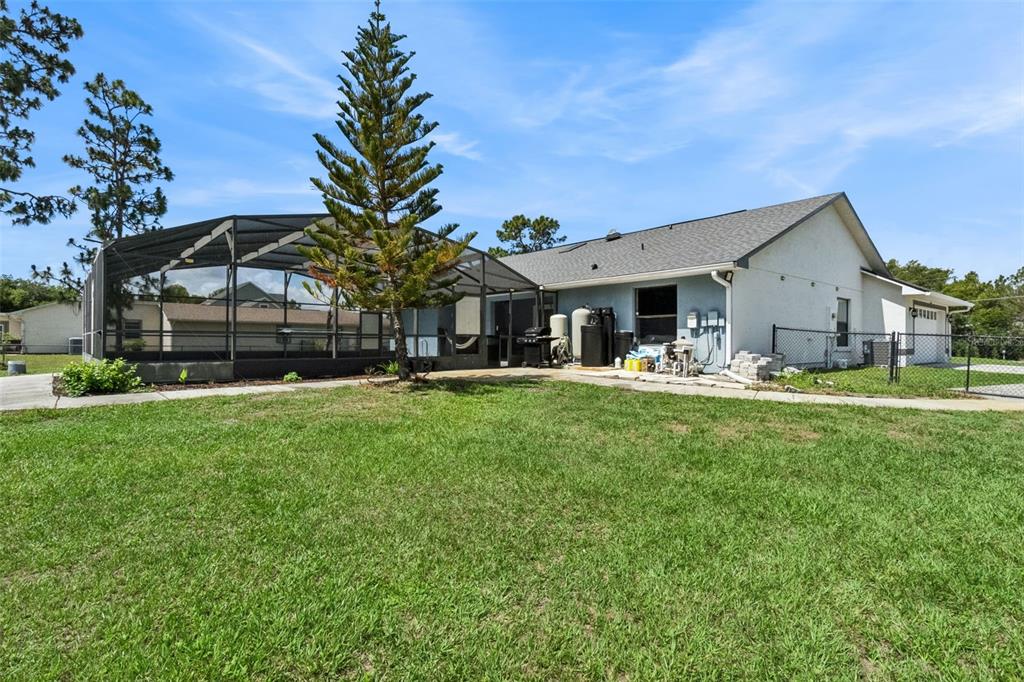 A backyard view of a house with a screened-in pool enclosure and a large tree — 7035 BIG BEND DRIVE, ST CLOUD, FL